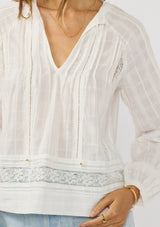 [Color: White] A detail image of a brunette model wearing a plaid sheer blouse with lace and pintuck details. Featuring a split v-neckline, dainty tie neck detail, and long sleeves. 