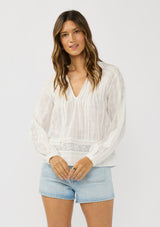 [Color: White] A front facing image of a brunette model wearing a plaid sheer blouse with lace and pintuck details. Featuring a split v-neckline, dainty tie neck detail, and long sleeves. 