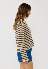 [Color: Tan/Navy] A  side facing image of a brunette model wearing a tan and navy striped sweater with open knit details, collar, and button front.