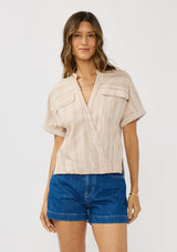 [Color: Sand/White] A front facing image of a brunette model wearing a cotton striped top with a surplice front, short dolman sleeves, and patch pockets.  
