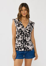 [Color: Vanilla/Black] A front facing image of a brunette model wearing an abstract floral print top with cap sleeves and a split v-neckline with ties. 