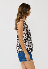 [Color: Vanilla/Black] A side facing image of a brunette model wearing an abstract floral print top with cap sleeves and a split v-neckline with ties. 