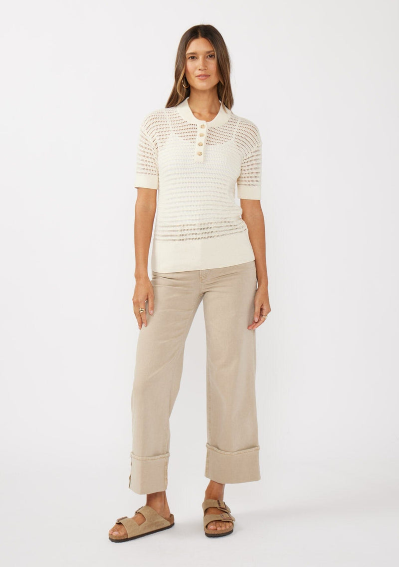 [Color: Vanilla] A front facing image of a brunette model wearing an off white cotton open knit top with short sleeves, ribbed trim, and a button front Henley placket.