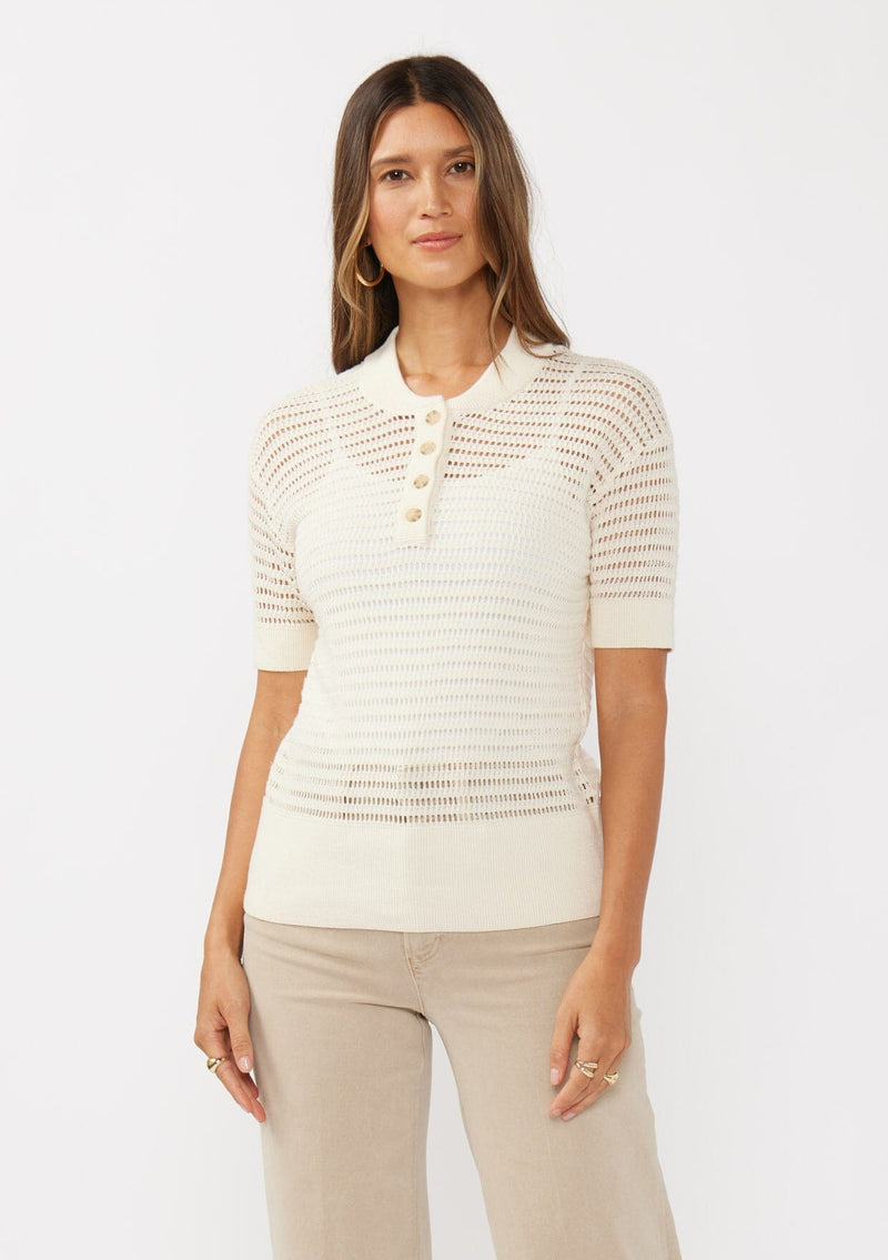 [Color: Vanilla] A front facing image of a brunette model wearing an off white cotton open knit top with short sleeves, ribbed trim, and a button front Henley placket.