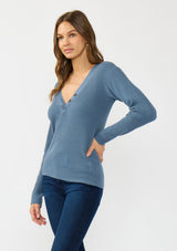 [Color: Heather Ocean] A side facing image of a brunette model wearing a blue waffle knit sweater top with a v neckline and a button front detail. 