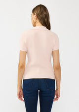 [Color: Light Pink] A back facing image of a brunette model wearing a light pink waffle knit polo top with a collared neck and button front. 