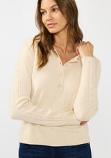 [Color: Stone] A front facing image of a brunette model wearing a beige sweater  polo with a button front, collared neck, and a cable knit detail on the sleeves. 