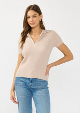 [Color: Heather Pearl] A front facing image of a brunette model wearing a light taupe waffle knit polo top with a collared neck and button front. 