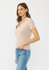 [Color: Heather Pearl] A side facing image of a brunette model wearing a light taupe waffle knit polo top with a collared neck and button front. 