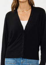 [Color: Black] A detail image of a brunette model wearing a black button front cardigan with long dolman sleeves, a v neckline, and rib trims. 