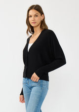 [Color: Black] A side facing image of a brunette model wearing a black button front cardigan with long dolman sleeves, a v neckline, and rib trims. 
