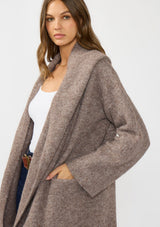 [Color: Heather Woodrose] A side facing image of a brunette model wearing a cozy wool blend coatigan with an oversized fit, hoodie, and side pockets. 