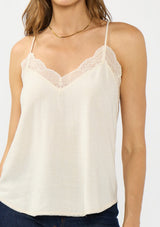 [Color: Vanilla] A detail image of a brunette model wearing a lace trimmed camisole with a v neckline and adjustable spaghetti straps. 