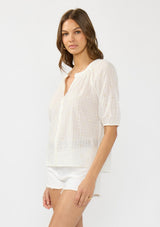 [Color: Natural/Cream] A side facing image of a brunette model wearing a white embroidered puff sleeve top with a button front. 