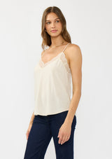 [Color: Vanilla] A side facing image of a brunette model wearing a lace trimmed camisole with a v neckline and adjustable spaghetti straps. 