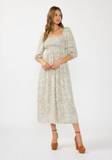 [Color: Dusty Sage/Natural] A front facing image of a brunette model wearing a green floral maxi dress with a mocked bust, three quarter sleeves, and a square neckline. 