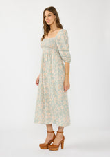 [Color: Dusty Sage/Natural] A side facing image of a brunette model wearing a green floral maxi dress with a mocked bust, three quarter sleeves, and a square neckline. 