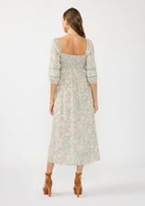 [Color: Dusty Sage/Natural] A back facing image of a brunette model wearing a green floral maxi dress with a mocked bust, three quarter sleeves, and a square neckline. 