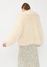 [Color: Vanilla] A back facing image of a brunette model wearing an ivory shaggy fur coat over a mint floral dress. 