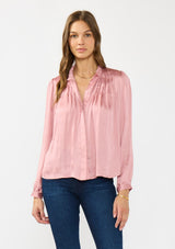 [Color: Rose] A front facing image of a brunette model wearing a pink silky poly satin blouse with pleats, a button front, and long sleeves. 