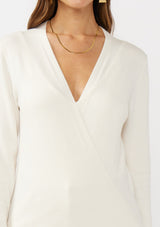 [Color: Off White] A detail  image of a brunette model wearing an off white solid knit sweater with a wrap front and side button closures. A soft versatile sweater, perfect for spring styling. 