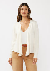 [Color: Off White] A front facing image of a brunette model wearing an off white solid knit sweater with a wrap front and side button closures. A soft versatile sweater, perfect for spring styling. 