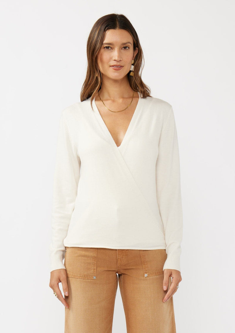 [Color: Off White] A front facing image of a brunette model wearing an off white solid knit sweater with a wrap front and side button closures. A soft versatile sweater, perfect for spring styling. 