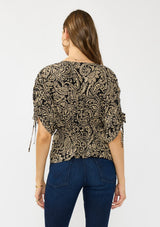 [Color: Black/Natural] A back facing image of a brunette model wearing a black and beige paisley print top with ruched sleeves, a v neckline, and an elastic peplum waist. 