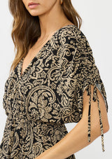 [Color: Black/Natural] A side facing image of a brunette model wearing a black and beige paisley print top with ruched sleeves, a v neckline, and an elastic peplum waist. 