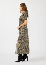 [Color: Black/Natural] A side facing image of a brunette model wearing a black and beige paisley maxi dress with short sleeves, a deep v neckline, and a side slit. 