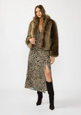 [Color: Black/Natural] A front facing image of a brunette model wearing a brown fur coat over a black and beige paisley maxi dress with short sleeves, a deep v neckline, and a side slit. 