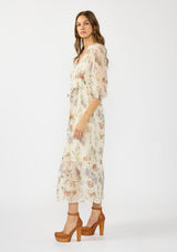 [Color: Ivory/Rosewood] A side facing image of a brunette model wearing an ivory floral midi dress with a waist belt, three quarter sleeves, and a v neckline. 