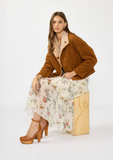 [Color: Ivory/Rosewood] A sitting image of a brunette model wearing a brown jacket with an ivory floral midi dress.