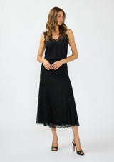 [Color: Black] A front facing image of a model wearing a black lace maxi skirt with black patent pumps. 