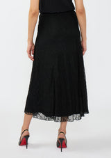 [Color: Black] A back facing image of a model wearing a black lace maxi skirt with black patent pumps. 