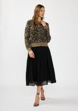 [Color: Brown] A front facing image of a brunette model wearing a brown leopard print cardigan with a button front, round neckline, and a contrast ribbed border. Styled with a flowy black maxi skirt. 