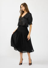 [Color: Black] A front facing image of a model wearing a black satin lace top with a crinkled black midi skirt.