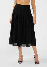 [Color: Black] A front facing image of a model wearing a crinkled black midi skirt with pleats. 