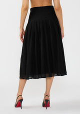 [Color: Black] A back facing image of a model wearing a crinkled black midi skirt with pleats. Styled with black patent pumps.