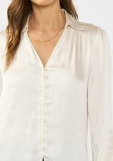 [Color: Eggshell] A detail image of a brunette model wearing a white satin blouse with a collar, v-neckline, button front, and long sleeves. 