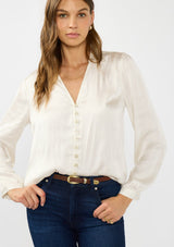 [Color: Eggshell] A front facing image of a brunette model wearing a white satin blouse with a collar, v-neckline, button front, and long sleeves. Tucked into a dark wash denim. 