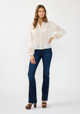 [Color: White/Sand] A front facing image of a brunette model wearing a white bohemian embroidered blouse with a button front. Styled with blue denim bottoms and brown block heels. 