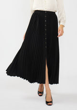 [Color: Black] A front facing image of a model wearing a black pleated maxi skirt with a button front and slit. 