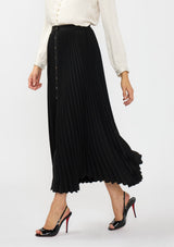 [Color: Black] A side facing image of a model wearing a black pleated maxi skirt with a button front and slit. 