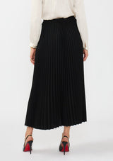 [Color: Black] A back facing image of a model wearing a black pleated maxi skirt with a button front and slit. 