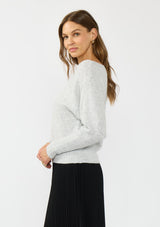 [Color: Heather Lunar] A side facing image of a brunette model wearing a light grey pullover sweater with an off shoulder design, boat neckline, and ribbed cuffs. 
