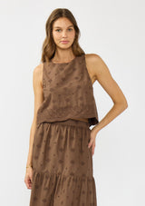 [Color: Brown] A front facing image of a brunette model wearing a brown crop tank top with tonal embroidery and a round neckline. Styled with a matching midi skirt. 