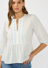 [Color: Light Blue/Cream] A front facing image of a brunette model wearing a white and blue embroidered blouse with a peplum silhouette, split v neckline, and three quarter length sleeves.