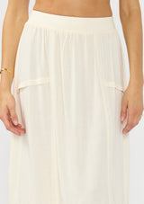 [Color: Natural] A detail image of a model wearing an off white midi skirt with lace trims and pintucks. 