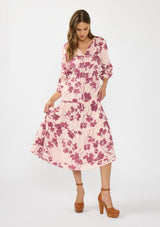 [Color: Coral/Wine] A front facing image of a brunette model wearing a three quarter sleeve midi dress with a pink and burgundy floral print, drawstring waist, and a tiered skirt. Styled with brown platform heels. 